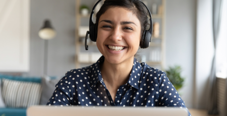 A smiling lady with headphones behind a laptop