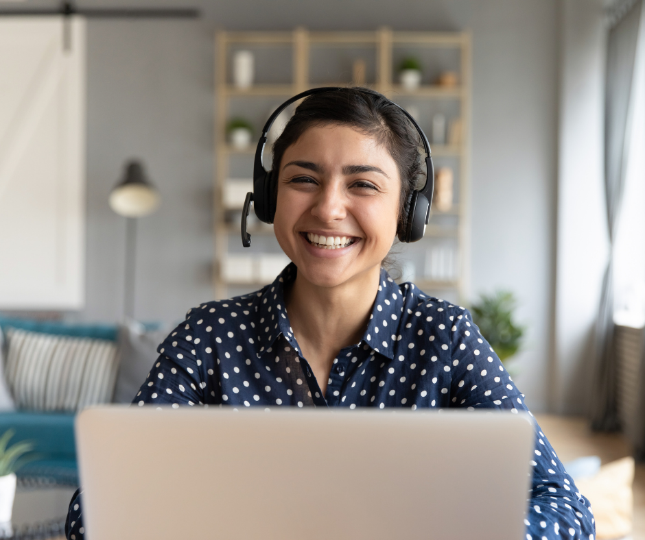A smiling lady with headphones behind a laptop