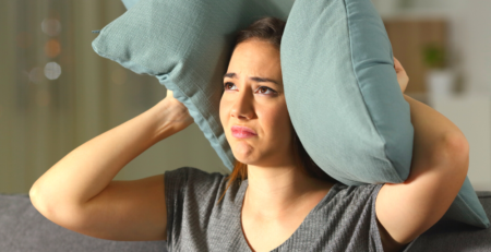 A distressed looking woman holding a pillow over her ear