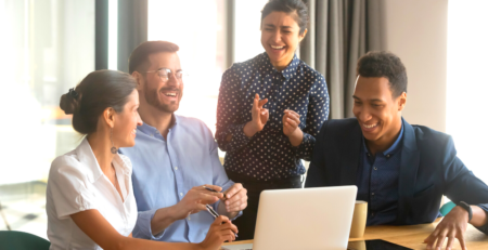 Four happy people behind a laptop looking relieved