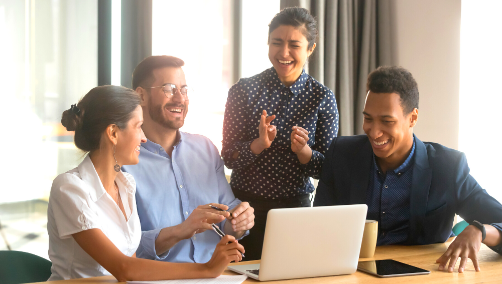 Four happy people behind a laptop looking relieved
