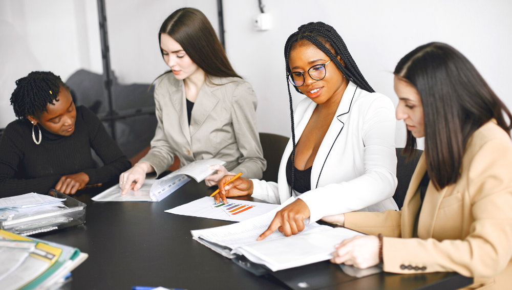 A diverse group of women discussing documents around a boardroom table