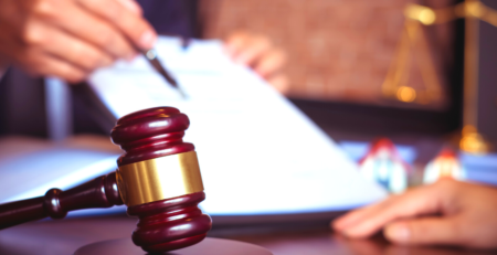 Legal gavel with a person with a pen in hand pointing to a document