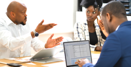 Three people in a meeting with one man looking angry